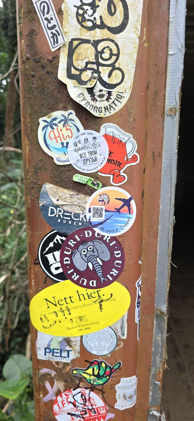 M and K Travel sticker among many stickers on a rusty trail post in Hawaii